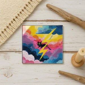 May include: Square glass coaster featuring a whimsical painting of a black cat silhouetted against a colorful sky with a yellow lightning bolt. The artwork includes shades of pink, blue, yellow, and white.