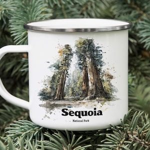 May include: White enamel mug featuring a watercolor illustration of giant sequoia trees. The mug has a silver rim and a white handle. The words "Sequoia National Park" are printed in black below the image.