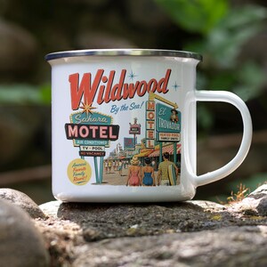A white ceramic mug with a colorful illustration of the Wildwood Motel, featuring various motel signs and a woman walking on a street.