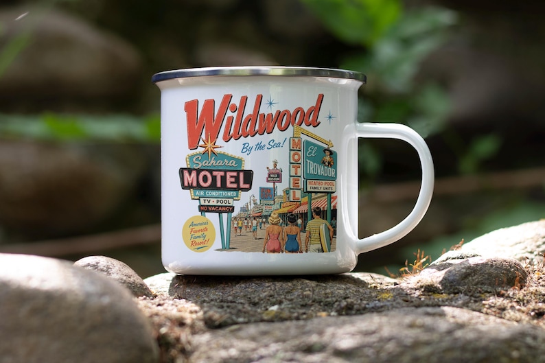 A white ceramic mug with a colorful illustration of the Wildwood Motel, featuring various motel signs and a woman walking on a street.