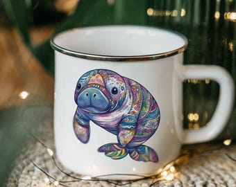 May include: White enamel mug with a colorful, patterned manatee design. The manatee is blue, purple, pink, and green. The mug has a silver rim.