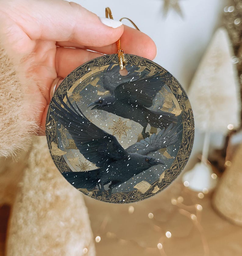 A hand is holding a circular ornament featuring a black bird with outstretched wings against a snowy background, with a star visible in the top right corner.