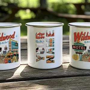 Three vintage-style mugs with the text "Wildwood By the Sea" printed on them, placed on a wooden surface.