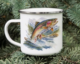 Puede incluir: Taza de esmalte blanco con borde plateado, con una colorida ilustración de una trucha arcoíris saltando del agua. La obra de arte incluye montañas y una escena de río, sobre un fondo de ramas de coníferas.