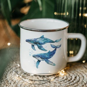 May include: White enamel mug with a silver rim featuring a watercolor illustration of two blue whales swimming.