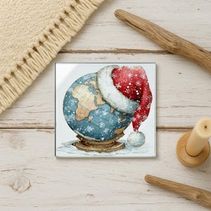 May include: Square glass coaster featuring a watercolor globe design with a Santa hat. The globe is blue with brown continents and white snowflakes. The Santa hat is red with white trim and snowflakes. A festive holiday decoration.