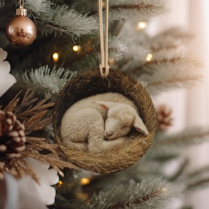 May include: A round Christmas ornament featuring a sleeping lamb nestled in a bed of hay. The lamb is white, and the ornament has a brown, woven border. The ornament hangs from a gold string, and is set against a blurred Christmas tree background.
