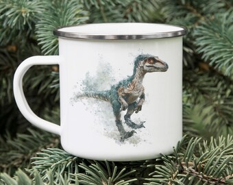 May include: White enamel mug with a silver rim and a white handle. The mug features a watercolor illustration of a blue and brown dinosaur. The dinosaur is in a running pose. The mug is set against a backdrop of green pine needles.