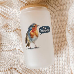 May include: A frosted glass tumbler with a wooden lid. The tumbler features a watercolor illustration of a robin with a speech bubble that says "No Comment". The bird has blue, orange, and brown feathers.