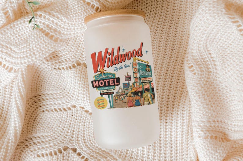 A white candle jar with a vintage-style label that reads "Wildwood by the Sea" and features an illustration of a motel and people.