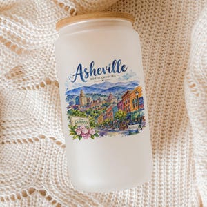 A frosted glass jar with a label depicting a scenic cityscape of Asheville, North Carolina.