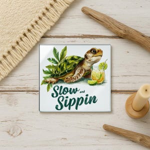 May include: Square glass coaster featuring a watercolor illustration of a sea turtle with a cocktail. The coaster has the words "Slow and Sippin" in green script. The turtle is surrounded by green leaves and a lime wedge.