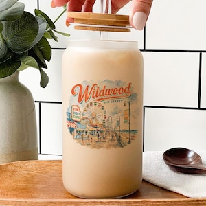 A hand is opening a glass jar with a Wildwood New Jersey design, surrounded by various objects such as a vase, a spoon, and a bottle.