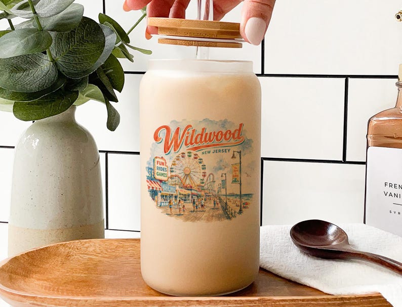 A hand is opening a glass jar with a Wildwood New Jersey design, surrounded by various objects such as a vase, a spoon, and a bottle.