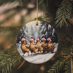 May include: A round Christmas ornament featuring a winter scene with five chickens wearing Santa hats pulling a sleigh through the snow. The ornament is suspended by a gold string and set against a blurred evergreen background.