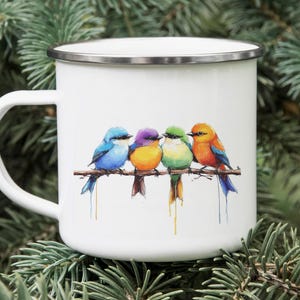 May include: White enamel mug with a silver rim and handle. The mug features a watercolor illustration of four colorful birds perched on a branch. The birds are blue, purple, green, and orange.