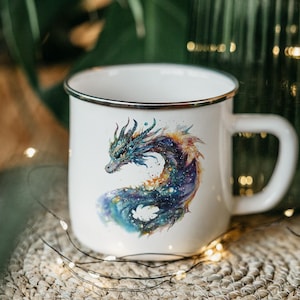 May include: White enamel mug with a silver rim featuring a watercolor illustration of a blue and purple dragon with a galaxy design.