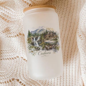 A frosted glass jar with a landscape scene printed on it, placed on a white knitted blanket.