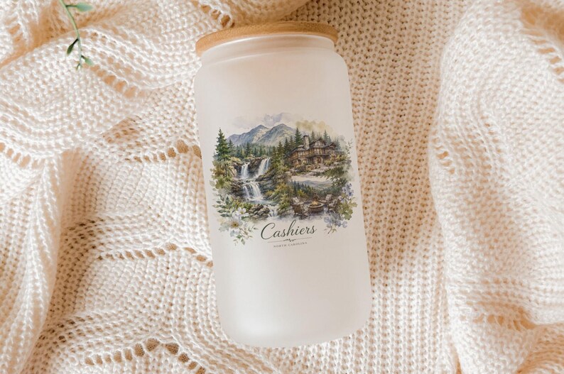 A frosted glass jar with a landscape scene printed on it, placed on a white knitted blanket.
