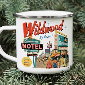 A white mug with a vintage-style illustration of a motel called Wildwood by the Sea, featuring neon signs and people enjoying the beach.