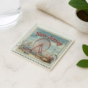 a coaster with a ferris wheel and a water glass on a marble surface, along with a potted plant and a leaf.