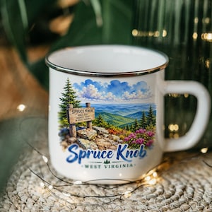 May include: A white enamel mug with a silver rim featuring a colorful illustration of Spruce Knob, West Virginia. The graphic shows a wooden sign reading Spruce Knob 4863 feet, a mountain landscape, pine trees, and the text Spruce Knob West Virginia.