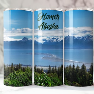 May include: A stainless steel tumbler with a colorful image of a mountain range and a body of water. The text "Homer Alaska" is printed on the tumbler.