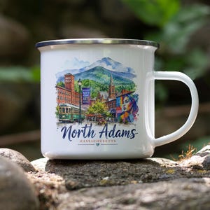 May include: A white enamel mug with a silver rim and a handle, featuring a colorful watercolor illustration of North Adams, Massachusetts, including a trolley, buildings, a mountain, and the text North Adams Massachusetts with a small heart icon.