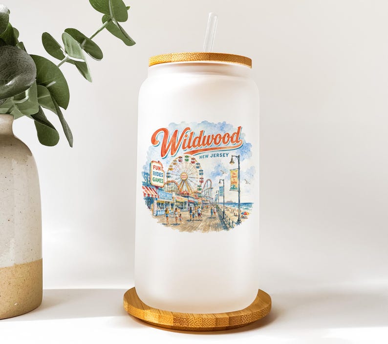 A glass jar with a printed design of a beach scene and a ferris wheel, placed on a wooden coaster.