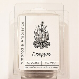 May include: A white soy wax melt with a campfire illustration and the text "Campfire" and "Ambrosia Ambiance". The wax melt is packaged in a clear plastic clamshell and weighs 2.5 ounces (70.9 grams).