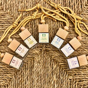 May include: A collection of small, rectangular glass bottles with wooden caps, each labeled with a different word like "Loving Essence" and "Radiant Power." The bottles are connected by a tan cord, arranged on a woven surface.