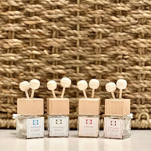 May include: Four small glass bottles with wooden tops and decorative wooden accents. Each bottle has a label with a different scent name: "earthen light", "rosemary mist", "citrus calm", and "bohemian bloom". The bottles are 1.7 oz each.
