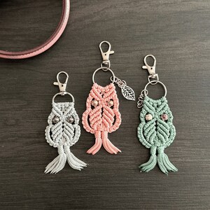May include: Three owl-shaped keychains with silver key rings. The owls are made of macrame and have silver beads for eyes. One owl is pink, one is green, and one is gray.