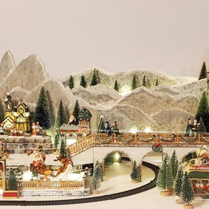 May include: A miniature Christmas village scene with a train track, houses, trees, and mountains. The houses have lit windows, and the scene is decorated with miniature figures and lights. The train is brown and black.