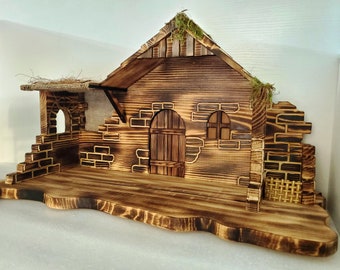 May include: A rustic wooden nativity scene with a weathered appearance. The structure features a wooden door, arched window, and a thatched roof with moss accents. The base is a wooden platform.