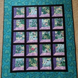 May include: A teal blue quilt with a black and purple frame. The quilt is made up of 16 squares, each with a different underwater scene.