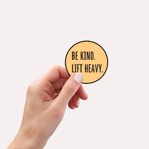 May include: A round, yellow sticker with black text that reads "Be Kind. Lift Heavy."