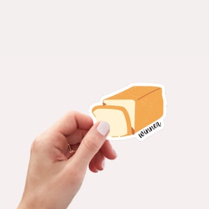 May include: A white sticker with a cartoon illustration of a loaf of bread with a slice cut out. The text "winner" is written below the bread.
