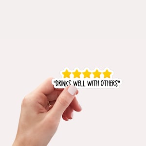 May include: A white sticker with five yellow stars and the text "DRINKS WELL WITH OTHERS".