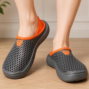 May include: A pair of dark gray clogs featuring a perforated mesh upper, a bright orange trim around the collar, and a matching orange heel strap. Each shoe displays a small orange patch on the side with the word SPORT embossed in black lettering.