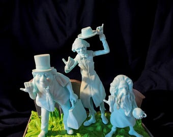 May include: A set of four ghostly figures from the Haunted Mansion attraction. The figures are made of a translucent blue plastic and are posed in a variety of humorous positions. The figures are standing on a green base with a brown border.