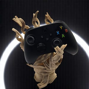 May include: A black Xbox controller with colorful buttons is held by a beige, wooden sculpture. The controller has the Xbox logo and a directional pad. The sculpture has a textured, organic appearance, with multiple arms and a head-like shape. The background is dark with a white halo.