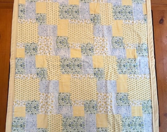 May include: A handmade quilt with a patchwork design. The quilt features squares of yellow, light blue, and floral patterned fabric. The quilt is bordered with a solid yellow fabric.