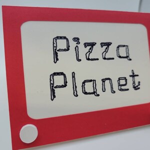 May include: Red and white sign with a white frame and a black inscription that reads "Pizza Planet".