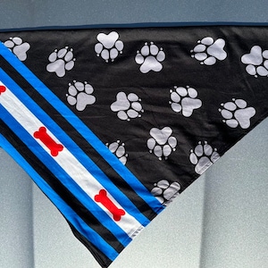Könnte beinhalten: Schwarzes Bandana mit weißen Pfotenabdrücken und roten Knochenmustern. Das Bandana hat ein blaues und weißes Streifenmuster mit einem blauen Rand. Das Bandana trägt den Text "PACKAPPEAL" in blau und weiß.