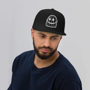 May include: A black and white flat brimmed baseball cap with a white smiling ghost design. The ghost has a striped pattern and a wide smile.