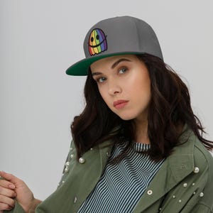 May include: A gray and green baseball cap with a rainbow ghost design. The ghost has a smiling face.
