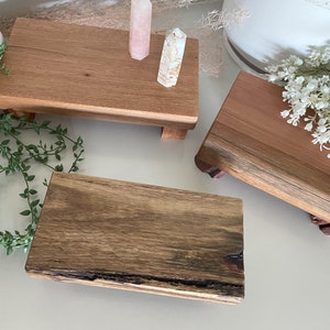 May include: Three rectangular wooden risers with short legs. One riser features a smooth, light brown grain, another has a reddish-brown tone, and the third displays a dark, textured live edge with visible wood grain patterns and natural knots.