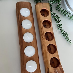 May include: Two rectangular wooden candle holders with natural live edges and a smooth finish. One holder contains five white tea light candles, while the other features five empty circular cutouts designed to hold tea light candles.