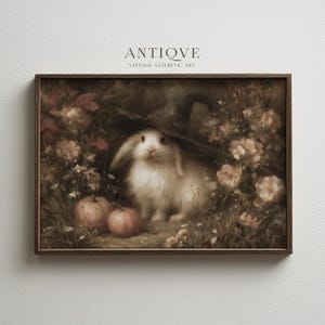 May include: A framed wall art print featuring a white rabbit wearing a dark pointed hat, surrounded by muted-toned flowers and two small pumpkins. The text ANTIQVE VINTAGE AESTHETIC ART is printed above the image in a dark, serif font.